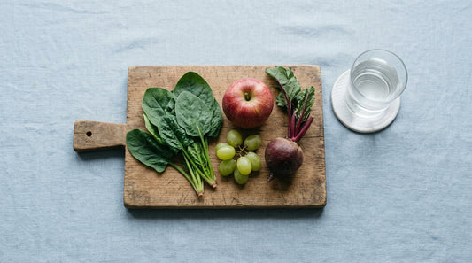 Spinach, apple, grapes and beet on a wooden board beside a glass of water