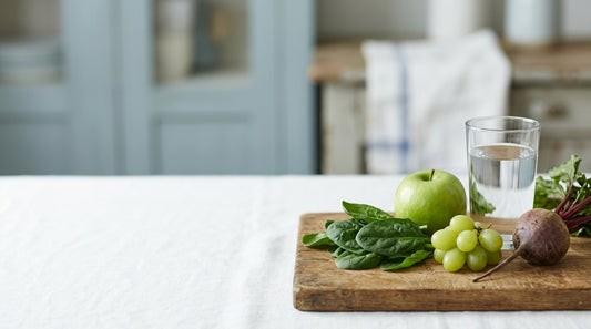 Spinach, apple, grapes and beet on a wooden board beside a glass of water
