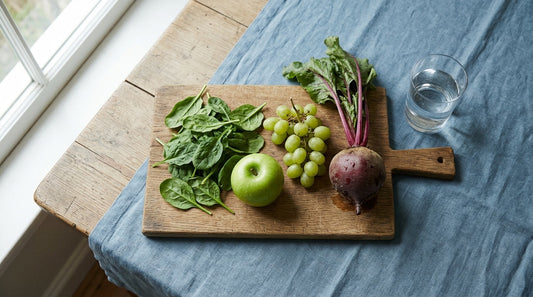 Spinach, apple, grapes and beet on a wooden board beside a glass of water