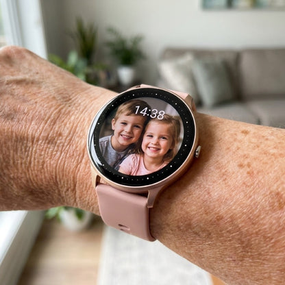 Close-up of the 360 Health Tracker on an older woman's wrist, the round screen showing a photograph of two young grandchildren as the watch face with the time 14:38